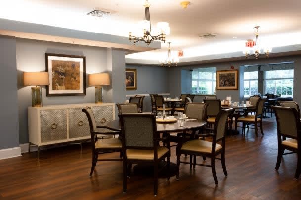 A cozy dining room with neatly arranged tables and chairs, featuring artwork on the walls and elegant lighting.