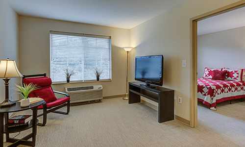 A minimalist living room with a TV, red chair, and floor lamp near a window.