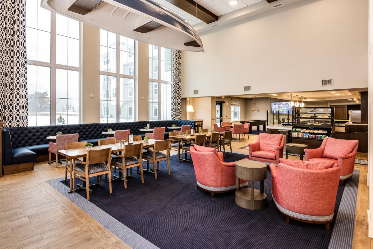 A modern restaurant interior with wooden tables, pink armchairs, and large windows providing ample natural light.