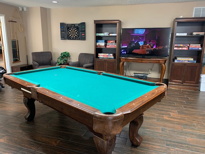 A cozy game room featuring a pool table and a large television, complete with comfortable seating and bookshelves.