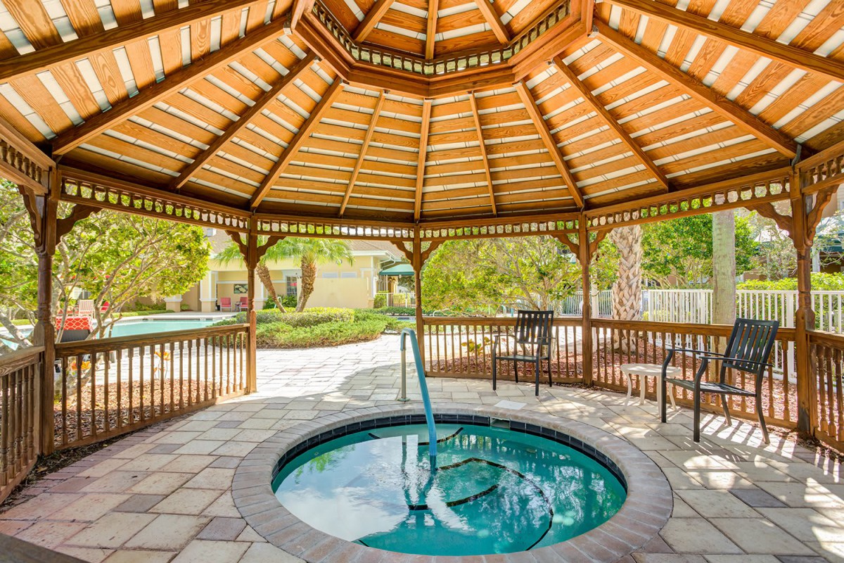 A wooden gazebo housing a hot tub in a serene garden setting.