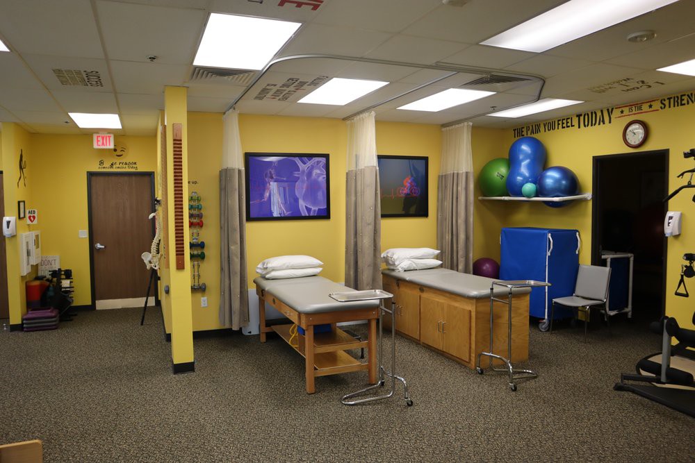 A physical therapy clinic room featuring treatment tables, exercise balls, and bright yellow walls.