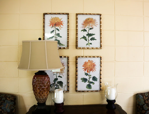A cozy corner featuring floral wall art, an elegant lamp, and candles.