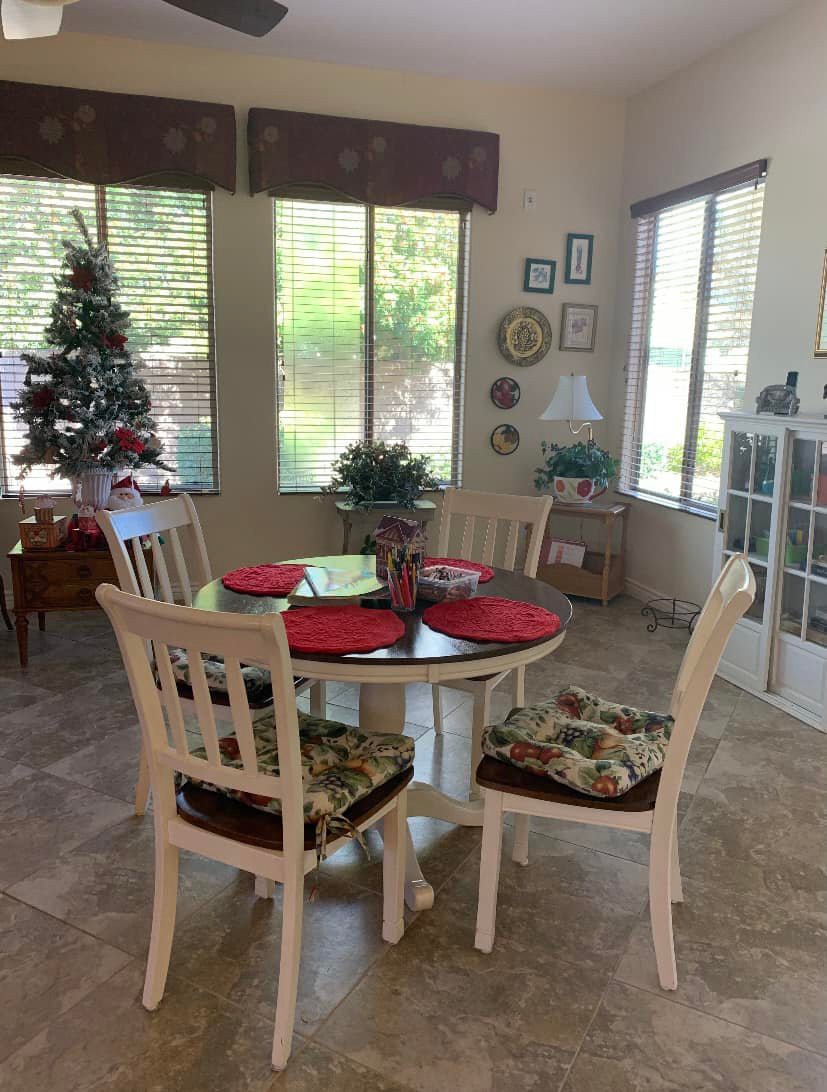 A cozy dining room with a round table set for four, featuring holiday decorations and a small Christmas tree by the window.