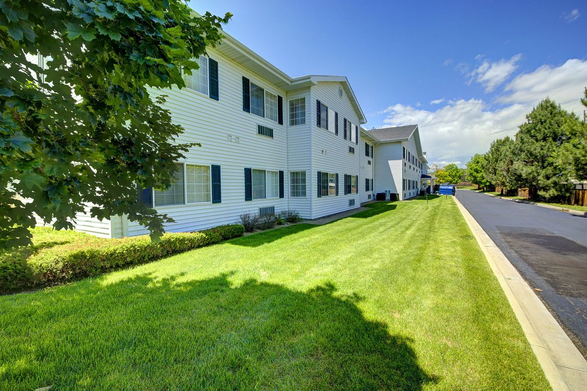 A residential building with a well-maintained lawn and trees under a clear blue sky.
