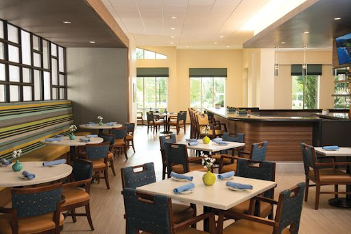 A bright and modern dining area featuring simple wooden tables and comfortable chairs, illuminated by natural light.