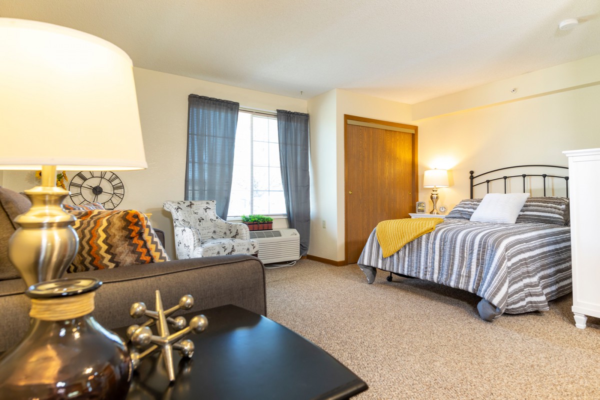 A cozy bedroom with stylish decor, featuring a bed, chair, and a large window letting in natural light.