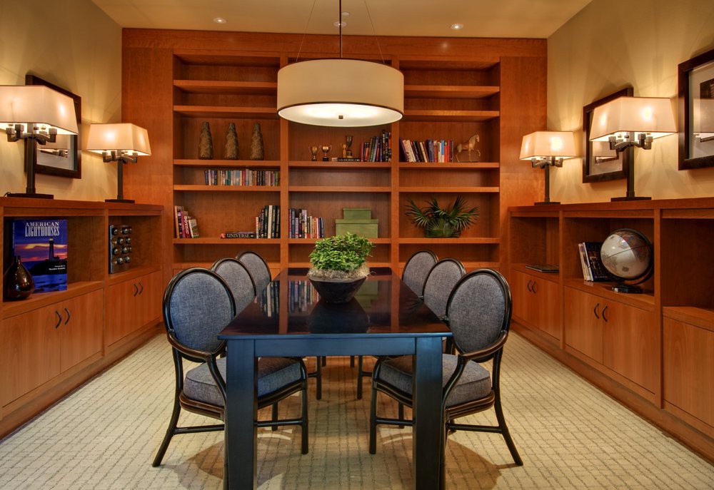 A modern dining room with a sleek table, upholstered chairs, and built-in bookshelves.