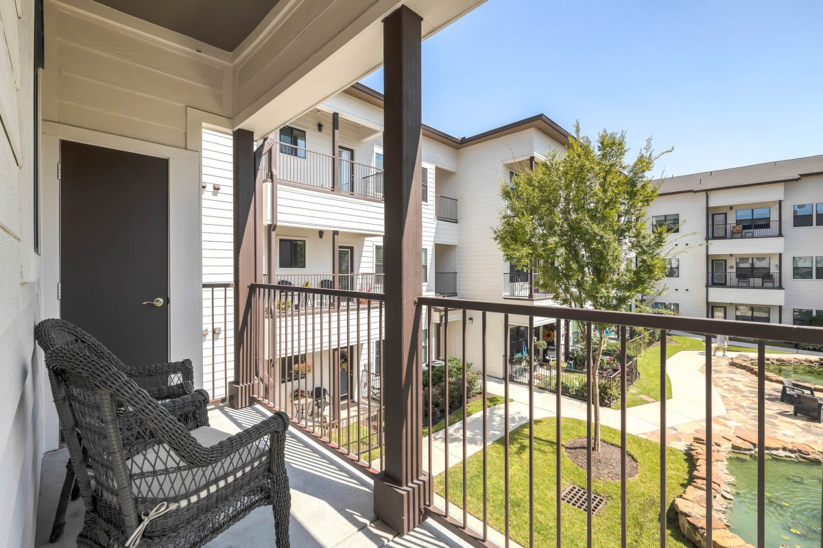 A sunny view from a balcony overlooking an apartment complex with outdoor seating.
