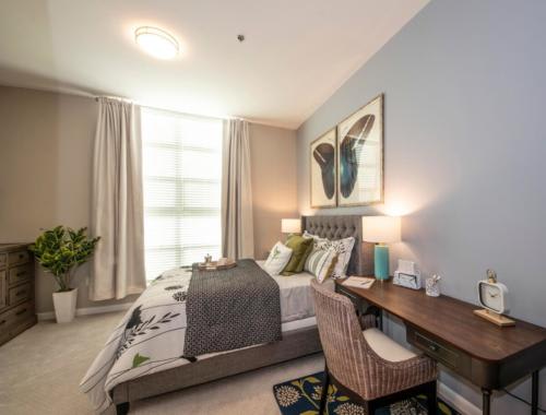 A cozy bedroom featuring a neatly made bed, a desk with a chair, and tasteful decor including artwork and lamps.