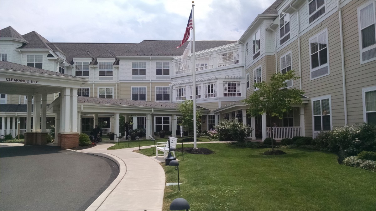 A well-maintained residential building with a driveway and a flagpole displaying a country flag.