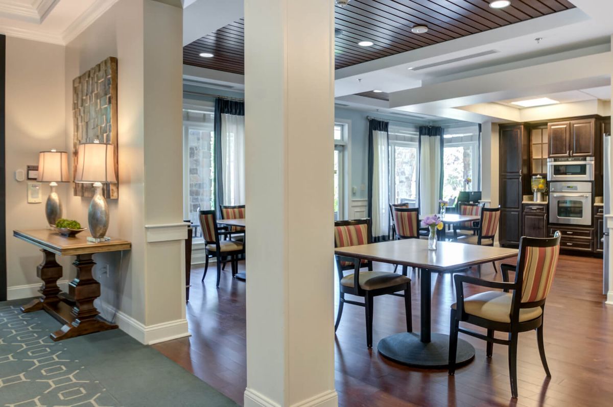A modern dining area with tables and chairs, featuring large windows and wooden flooring.