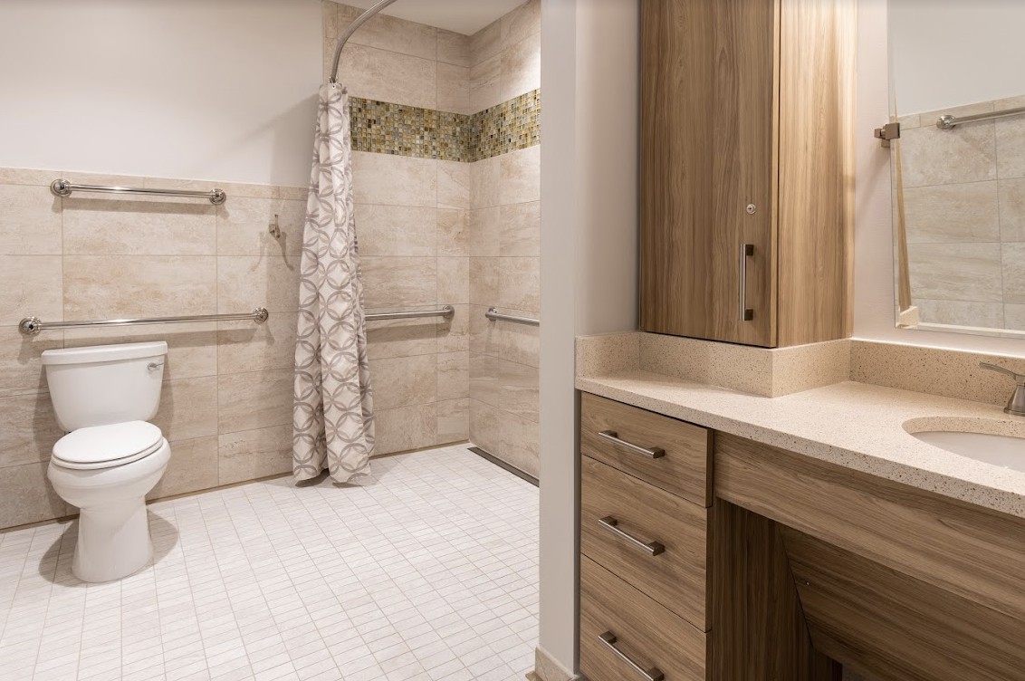 A modern bathroom features a spacious shower area with patterned tiles and grab bars, alongside wooden cabinets for storage.