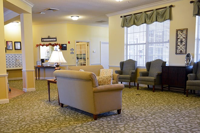 A cozy living room with a sofa, chairs, and a lamp on a carpeted floor.