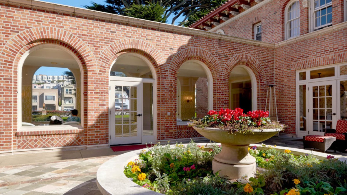 A charming brick building with arched windows surrounding a courtyard adorned with colorful flowers.