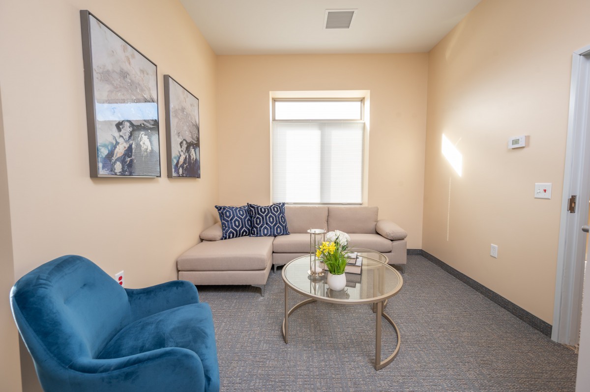 A modern living room with neutral tones, featuring a beige sofa and a blue armchair around a glass coffee table.