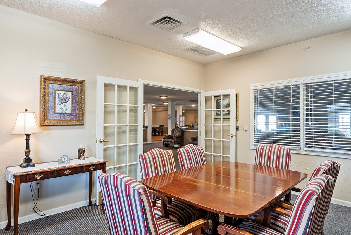 A conference room with a wooden table and striped chairs, separated by glass doors.