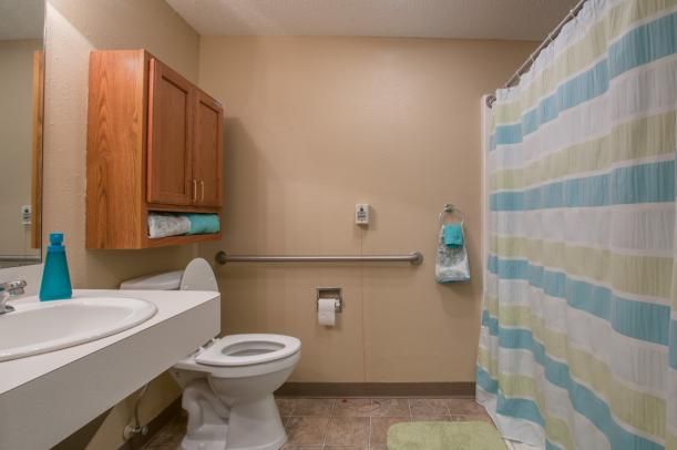 A bathroom with a toilet, sink, and striped shower curtain featuring wooden cabinets and a handrail.
