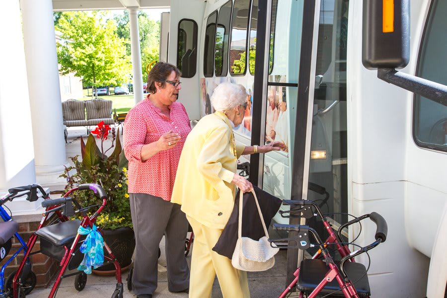 An elderly woman receives assistance while boarding a bus, using a walker for support.