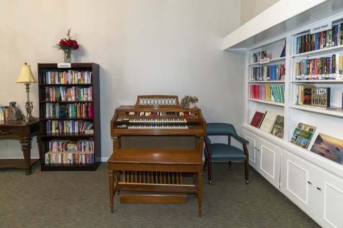 A cozy room featuring a vintage organ surrounded by bookshelves and a chair.