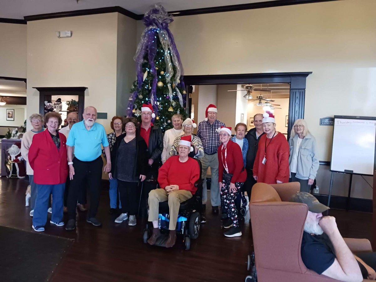 A group of people gathered indoors in front of a decorated Christmas tree, celebrating the holiday season.