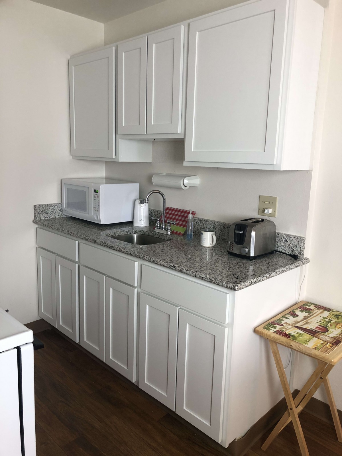 A compact kitchen area with white cabinets, featuring a microwave and toaster on the countertop.