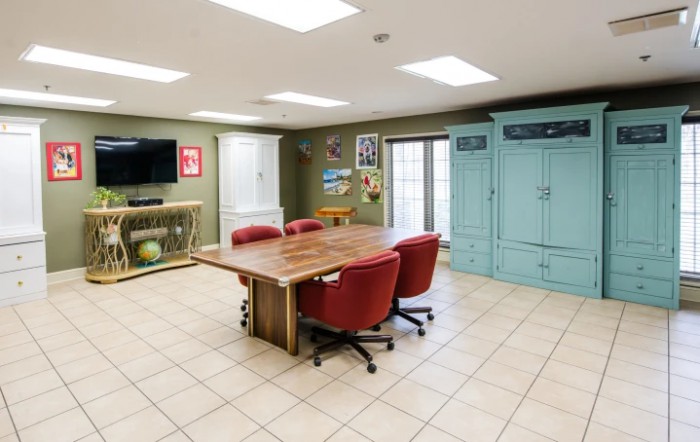 A modern conference room with a wooden table, red chairs, TV, and storage cabinets.