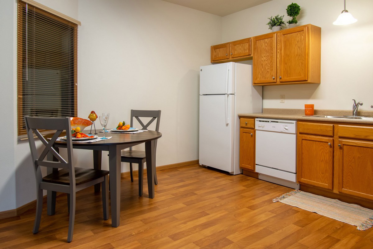 A cozy kitchen and dining area with wooden cabinets, a refrigerator, dishwasher, and a small dining table.