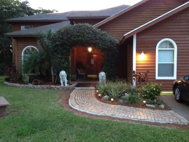 A welcoming house entrance with a lit pathway and lush greenery during the evening.