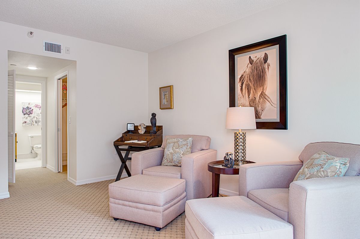 A cozy living room featuring neutral-colored armchairs, a lamp, and artistic wall decor.