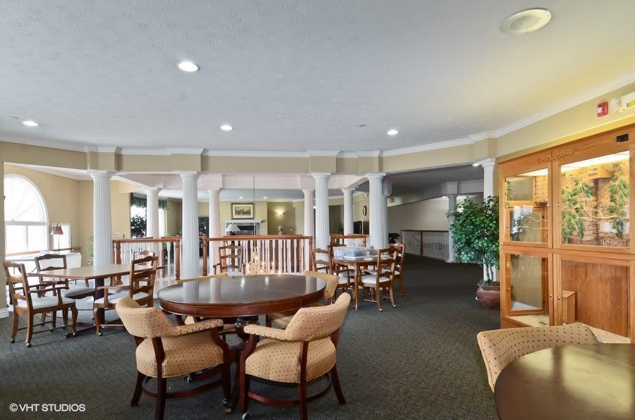 A spacious lounge area featuring several tables and chairs, accented by columns and a carpeted floor.