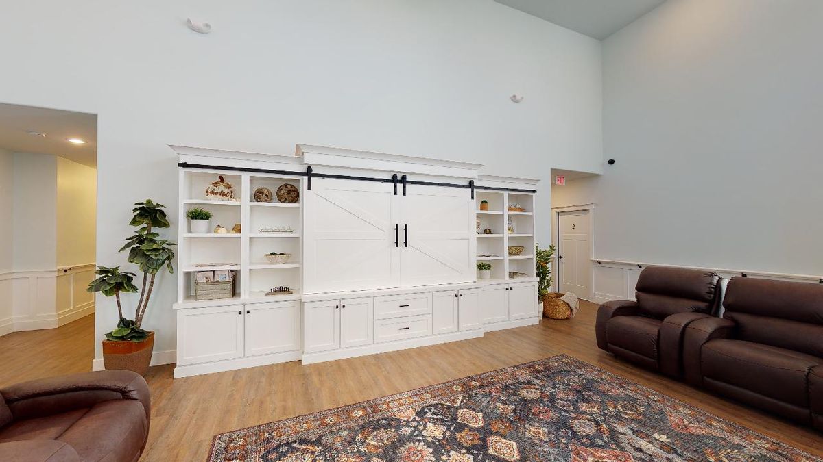 A spacious living room with white bookshelves and a cabinet featuring sliding doors, complemented by wood flooring and an area rug.