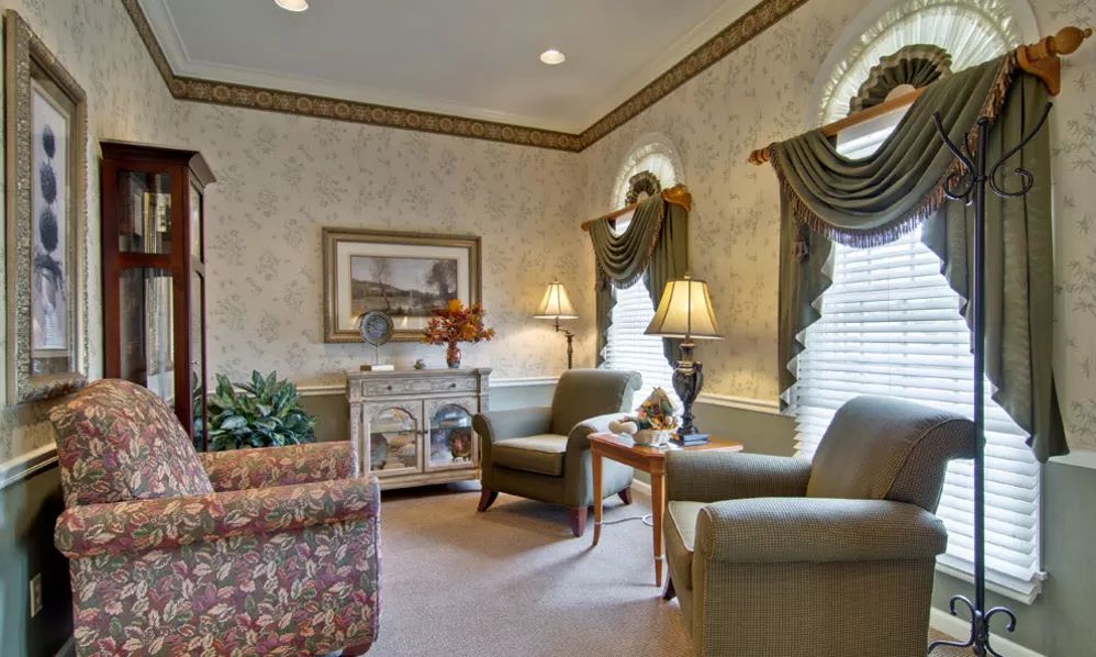 A traditionally decorated living room featuring comfortable armchairs, a floral sofa, and soft lighting.