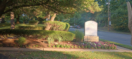 A peaceful cemetery setting with well-maintained hedges and flower beds, bathed in the warm glow of evening sunlight.