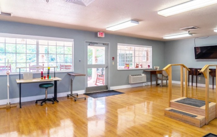 A spacious room in a rehabilitation center with exercise equipment and wooden flooring.
