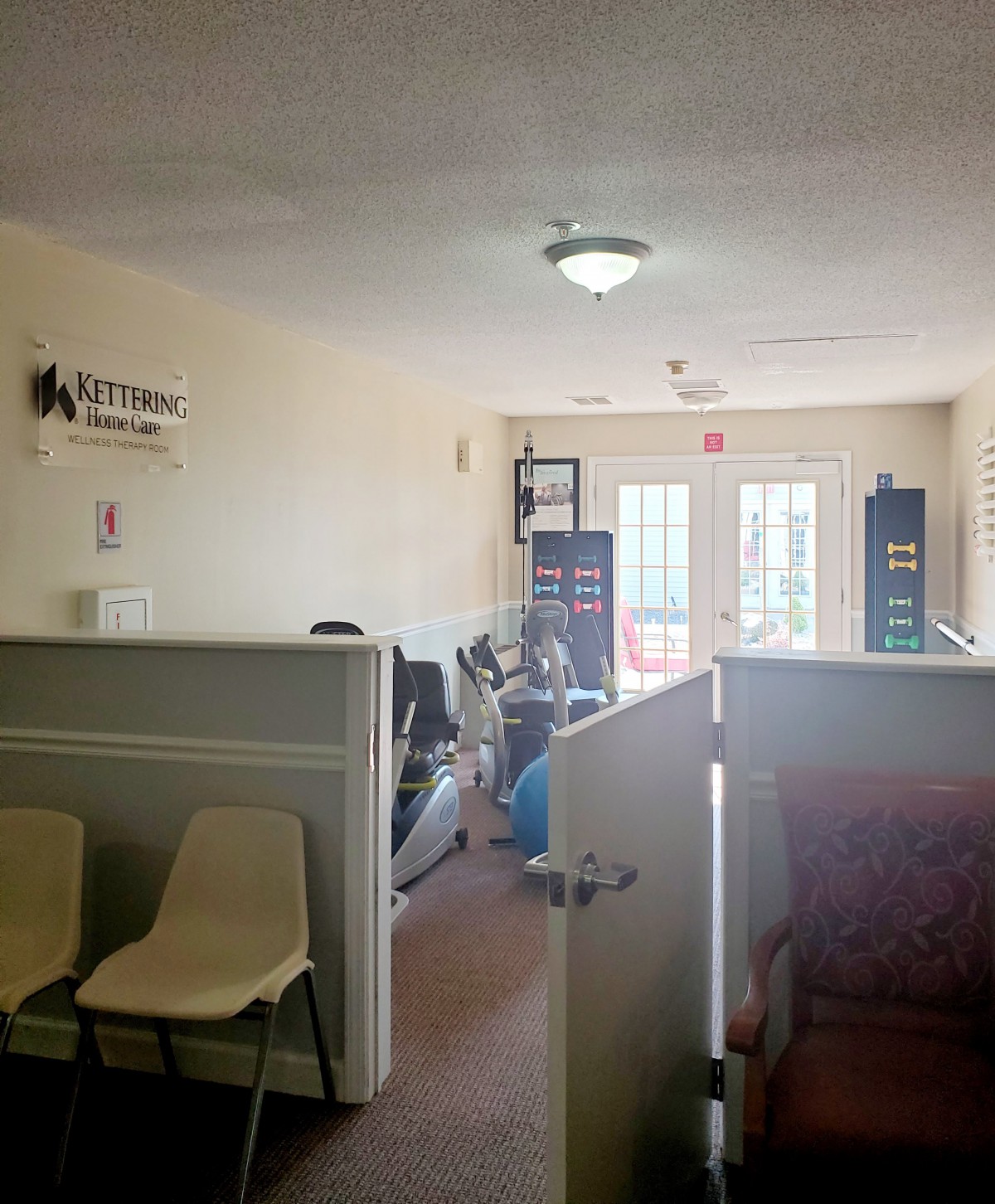 A small office interior with a waiting area, chairs, equipment, and natural lighting coming through the doors.