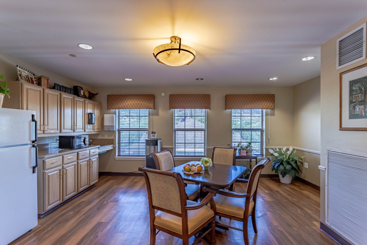 A cozy kitchen and dining area with wooden floors, a round table surrounded by chairs, and large windows letting in natural light.