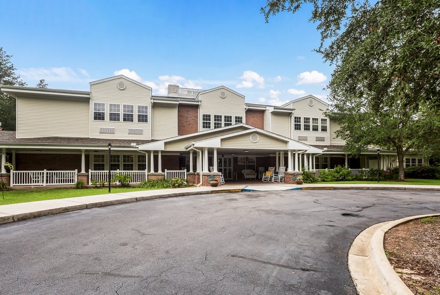 A large residential building with a driveway and surrounding trees under a clear blue sky.