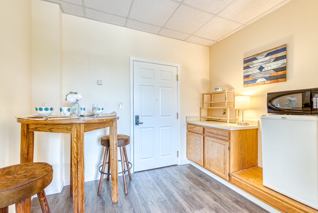 A cozy kitchenette area with wooden cabinets, a small bar table, and a stool, featuring minimalist decor.