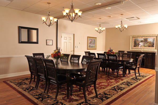 An elegant dining room with formal setup, featuring chandeliers and a decorative rug.