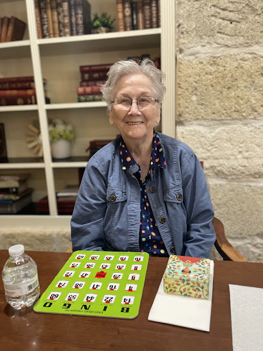 An elderly woman enjoying a game of bingo, smiling at the camera.