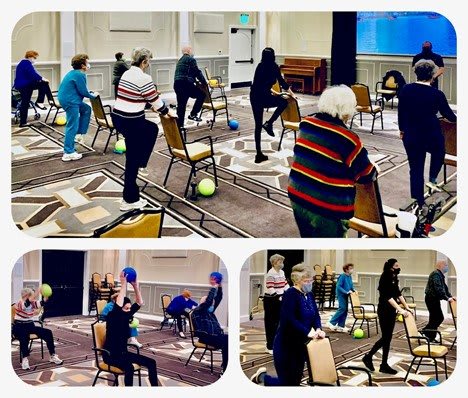 A group of seniors participating in an indoor exercise class using chairs.