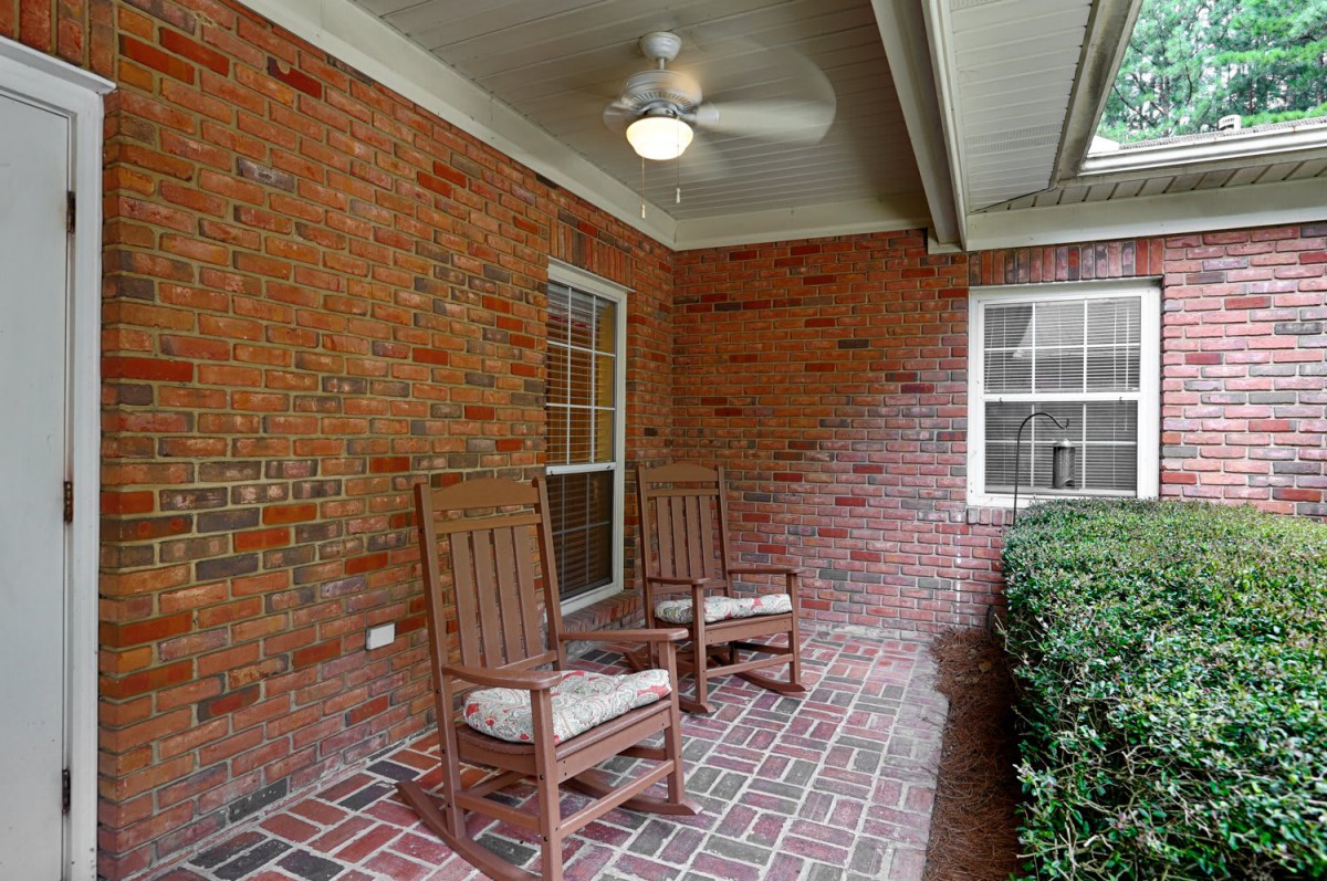 A cozy patio with two wooden chairs, a ceiling fan, and brick walls.