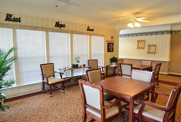 A cozy dining area with wooden tables and chairs, carpeted flooring, and decorative elements including wall art and plants.