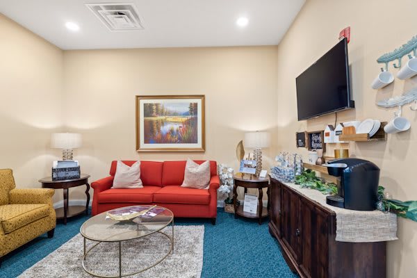 A cozy waiting room featuring a red sofa, coffee table, and a television.