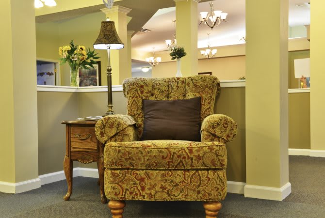 A cozy living room corner with an ornate armchair, side table, and lamp.
