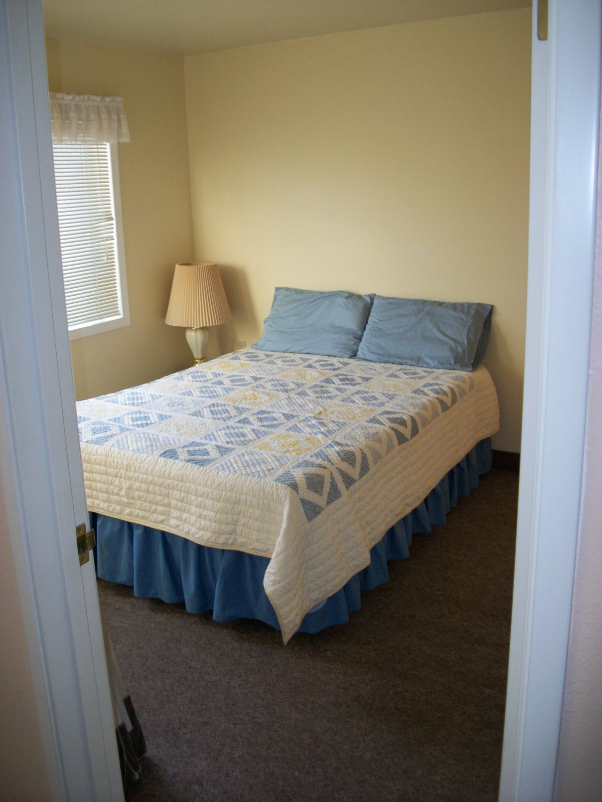 A cozy bedroom with a neatly made bed, complete with pillows and a quilt, beside a lamp and window.