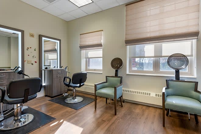 A well-lit hair salon with chairs, a mirror, and wooden flooring.