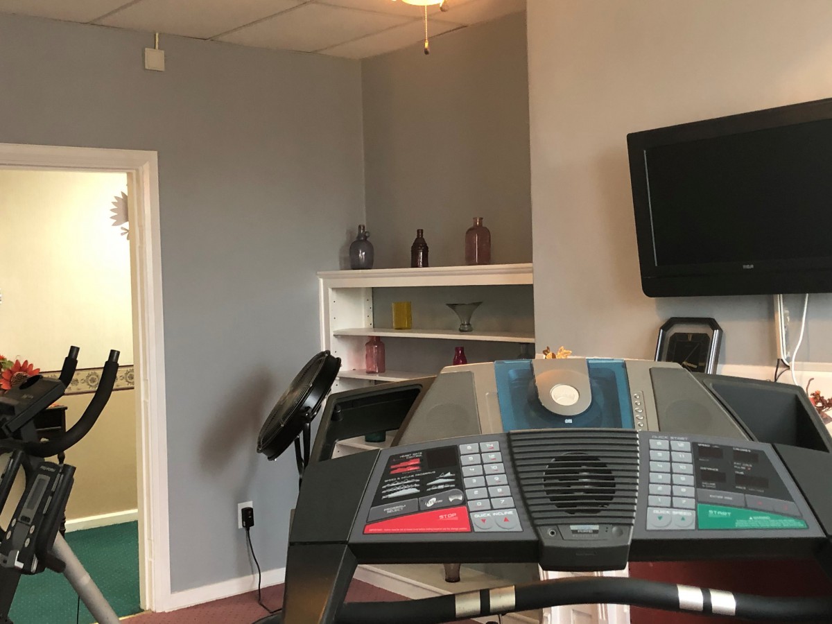 A small gym room with a treadmill, television, and shelves.