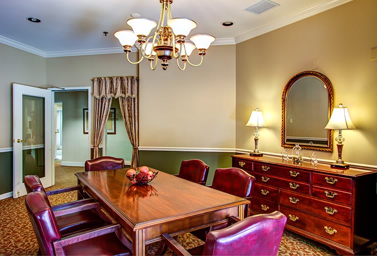 A classic dining room featuring a wooden table with red chairs, a chandelier, and a sideboard with a mirror.